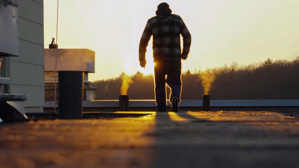 Roofing professional walking across a flat commercial roof during sunrise, inspecting vents and rooftop equipment.