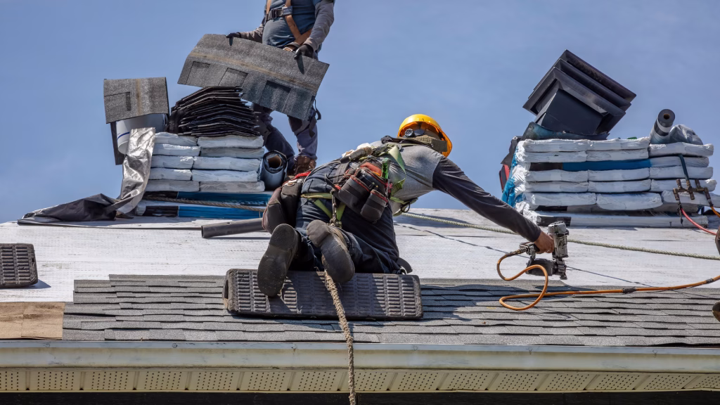 Construction Roofers with Nailer Installing Asphalt Shingles on Residential House Roof