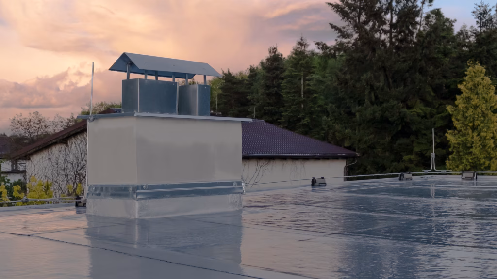 Flat roof covered with bitumen membrane and silver lacquer with chimney on a private house. Reflections after rain