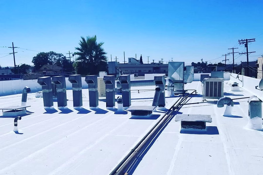 White reflective coating applied to a flat commercial roof with HVAC units and ventilation pipes, improving energy efficiency and weather protection.